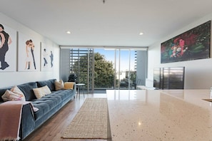 A modern living room with a sofa, a coffee table, and a large window. - Eden Terrace Oasis | Park Views, BBQ & Parking (Auckland Central Suburbs)