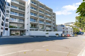 A multi-story residential building with balconies, a gated entrance, and parked cars. - Eden Terrace Oasis | Park Views, BBQ & Parking (Auckland Central Suburbs)