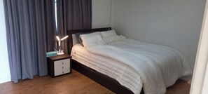 A bedroom with a bed, a nightstand, a lamp, and a window with curtains. - 3-Min Walk to Camp Humphreys Gate , Private Villa (Pyeongtaek)