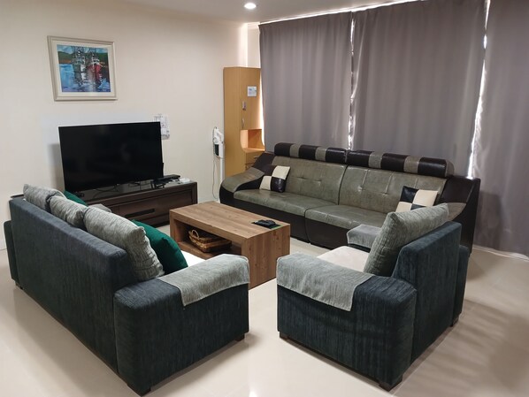 A living room with a sofa set, a coffee table, a flat-screen TV, and a painting on the wall.