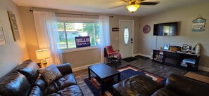 A living room with a leather couch, a coffee table, a TV, and a bookshelf. - 3-bedroom lake house in Hamburg, 10 minutes from Bills Stadium! (Hamburg)