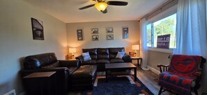Ein Wohnzimmer mit einer Couch, einem Sessel und einem Couchtisch, einem Deckenventilator und einem Fenster mit Blick.