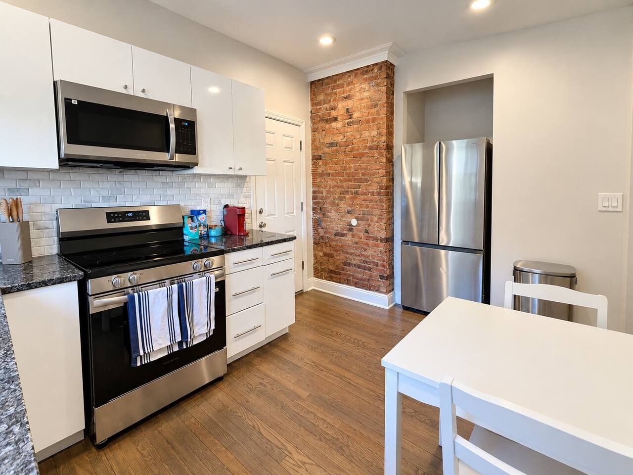 A modern kitchen with stainless steel appliances, wooden flooring, and a brick accent wall.