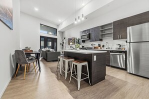 A modern kitchen with a central island, dark cabinetry, stainless steel appliances, and a dining area with bar stools. - Luxury 2BR Loft, Private Balcony, Free Parking + Gym (Cleveland)