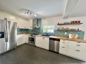Een moderne keuken met roestvrijstalen apparatuur, witte kastjes en een turquoise spatwand.