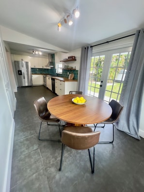 A modern kitchen with white cabinets, a stainless steel refrigerator, and a dining area with a round wooden table and leather chairs. - The Miami Urban House - Modern Serenity in the Heart of Miami (Miami)