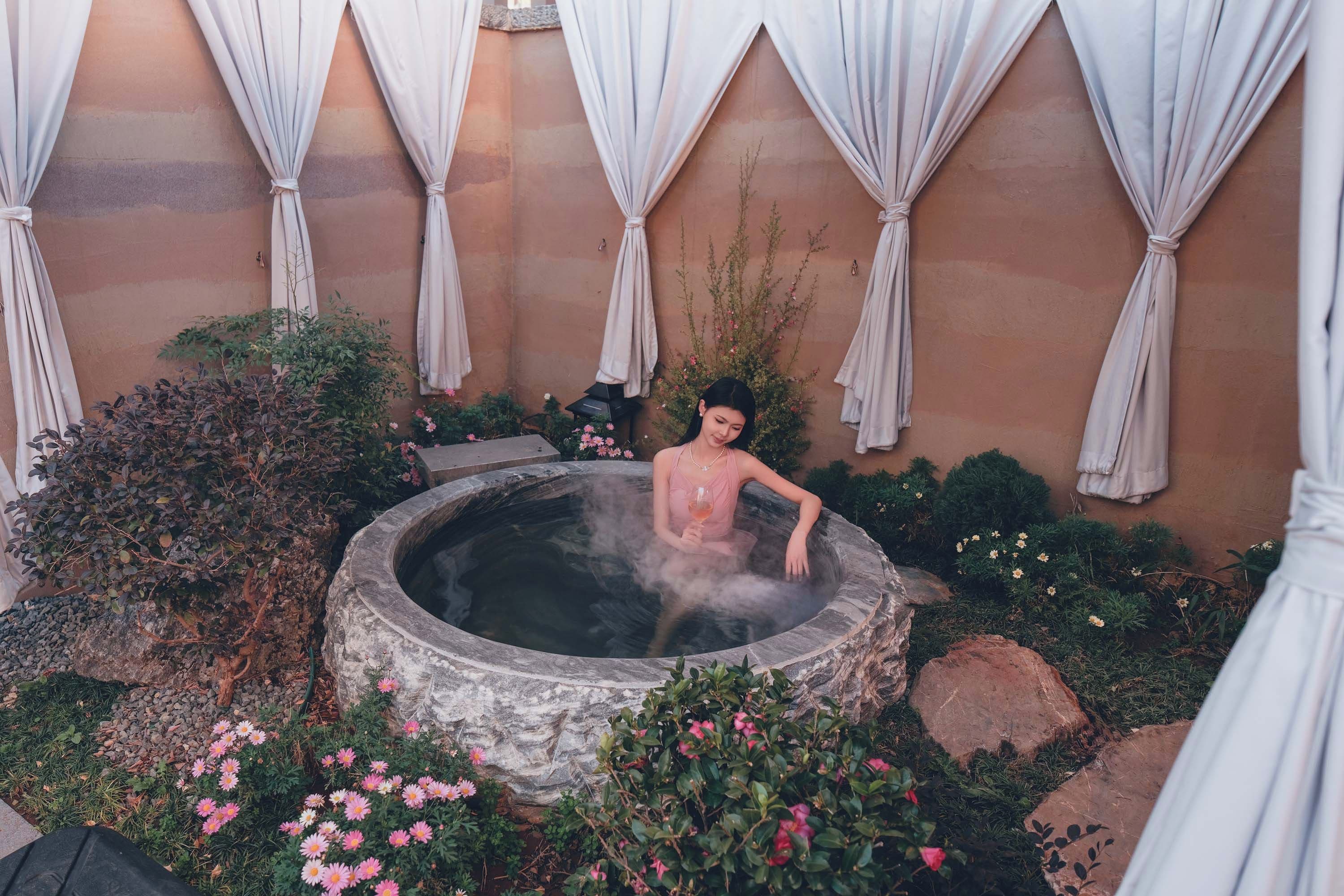 A person in a hot tub surrounded by greenery and flowers.