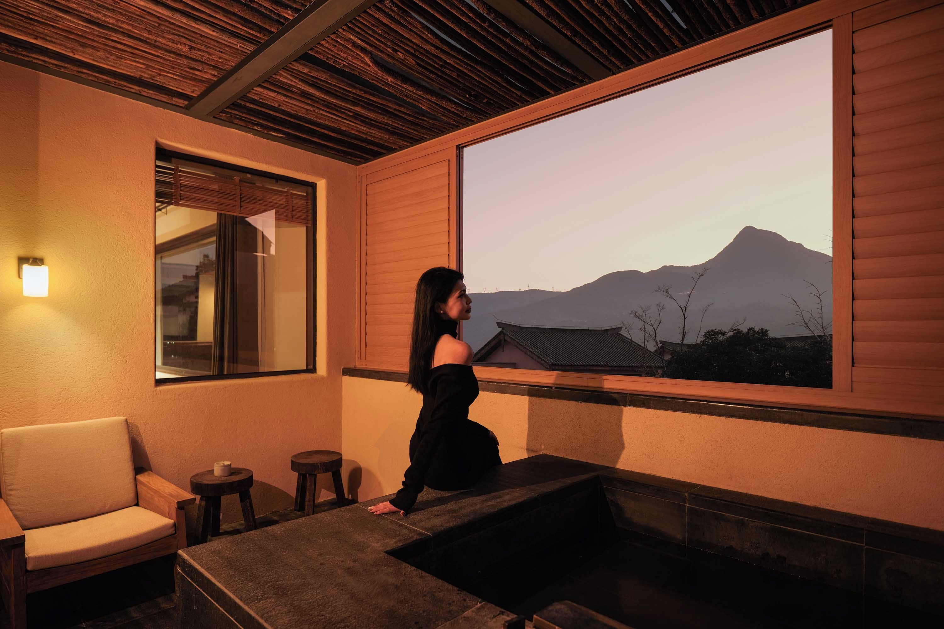 Una persona de pie junto a una ventana con vistas a un paisaje montañoso.