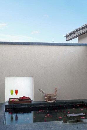 A rooftop pool with a clear sky, a wooden bucket, and a tray with fruits and drinks.