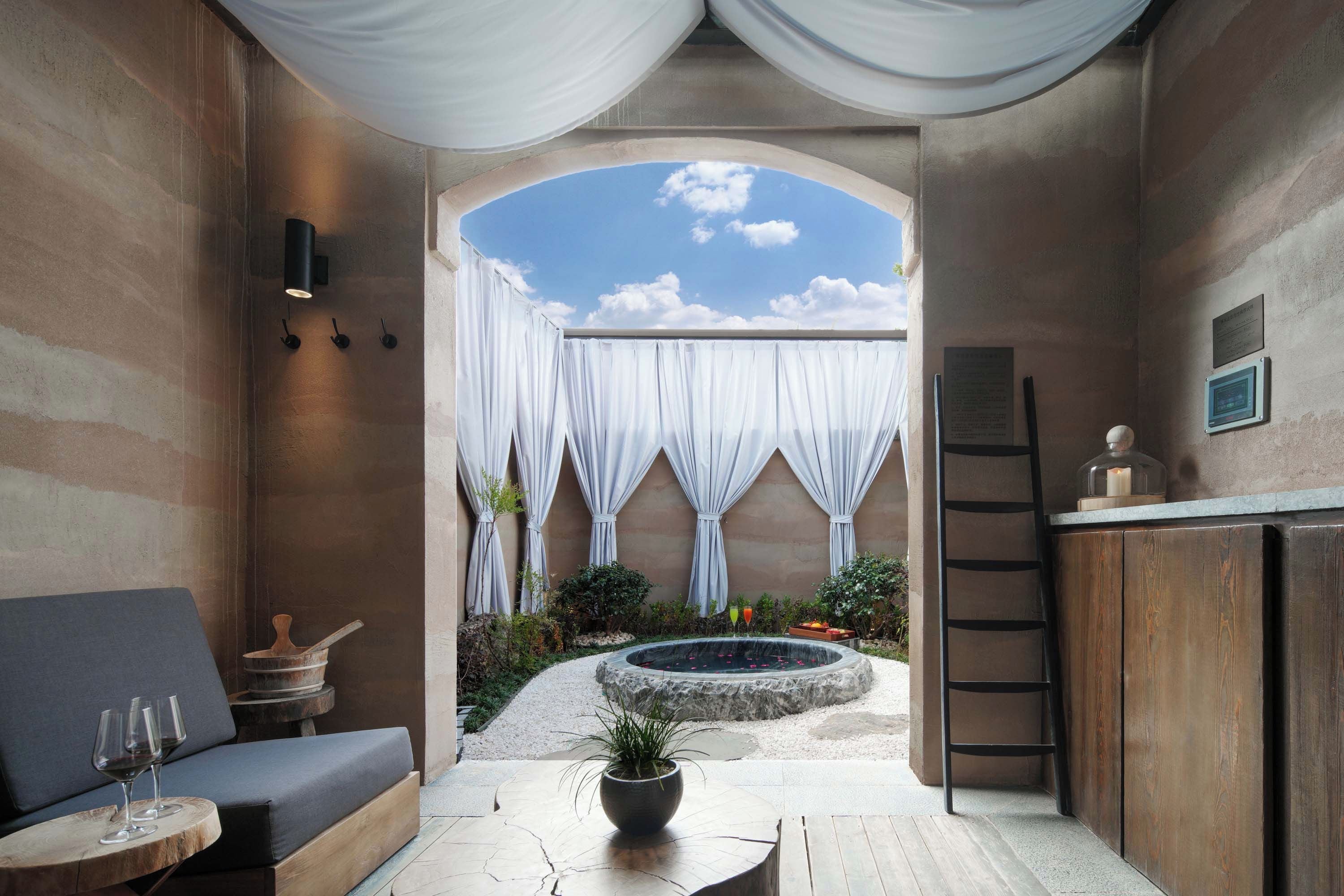 Un espacio interior acogedor con vista a un jardín, una zona de estar con mesa y sillas, y una pequeña fuente.