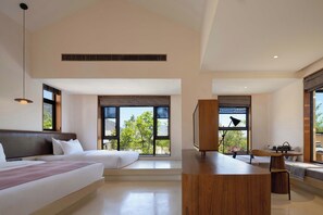 A modern hotel room with a large bed, a desk, and a view of greenery outside.