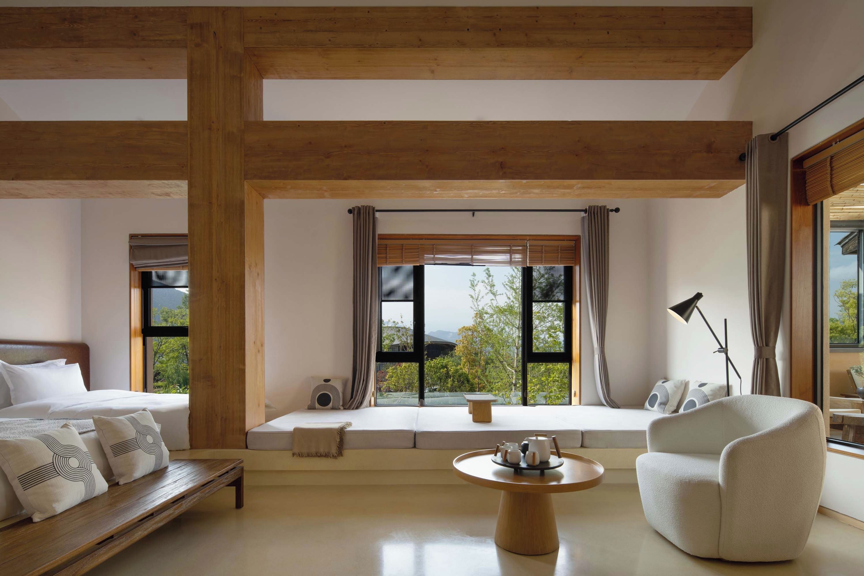 A modern room with a large window, wooden beams, a bed, a sofa, a table, and a chair.