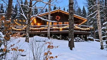 A wooden cabin with a deck, surrounded by snow-covered trees.
