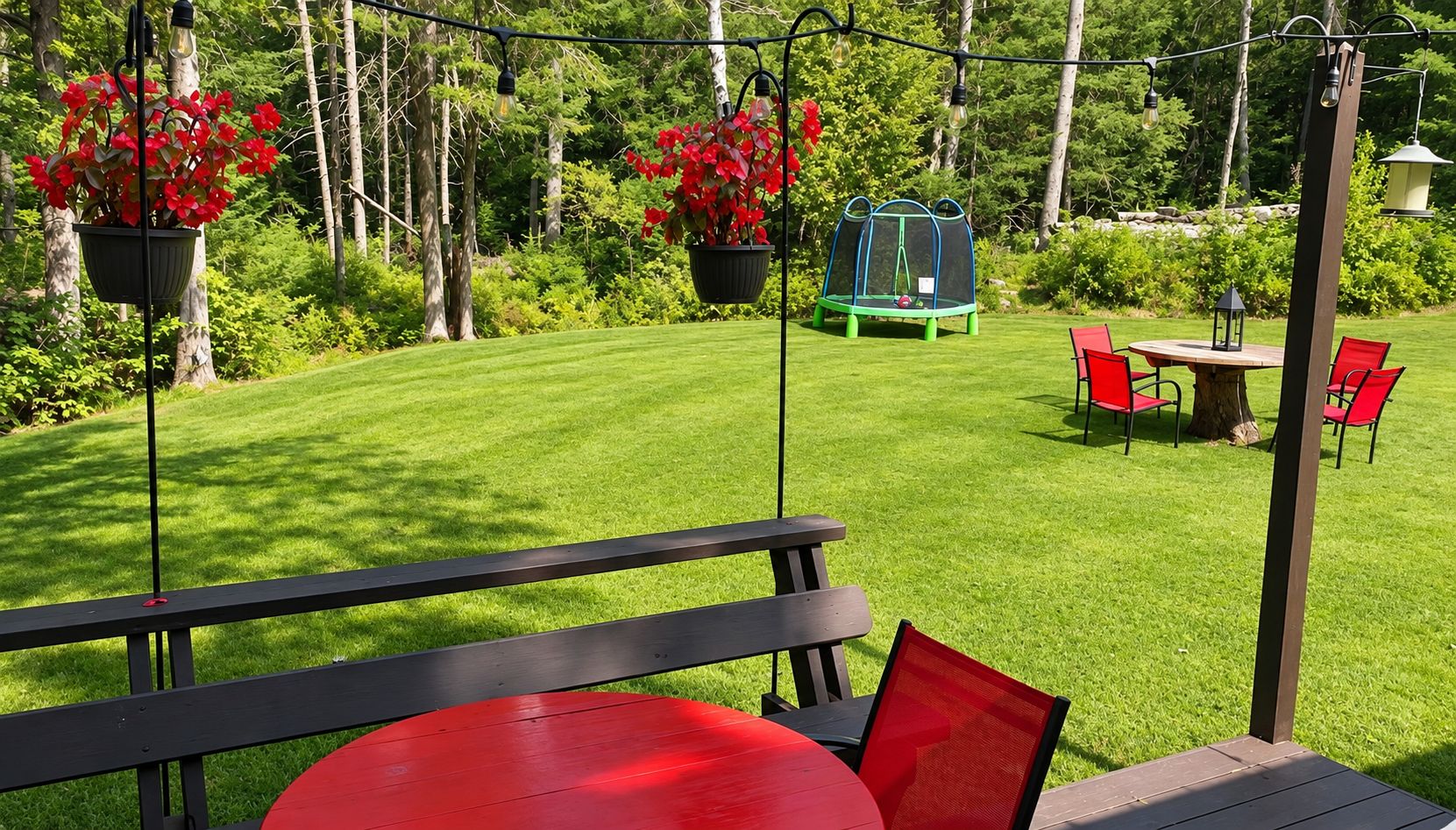 A patio with a table and chairs, surrounded by a well-maintained lawn and hanging planters with red flowers.