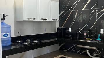 Cozinha com armários brancos, uma bancada de mármore preto e um dispenser de água azul.