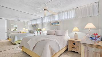 A hotel room with a large bed, two bedside tables, a ceiling fan, and a view of the sea through the window.