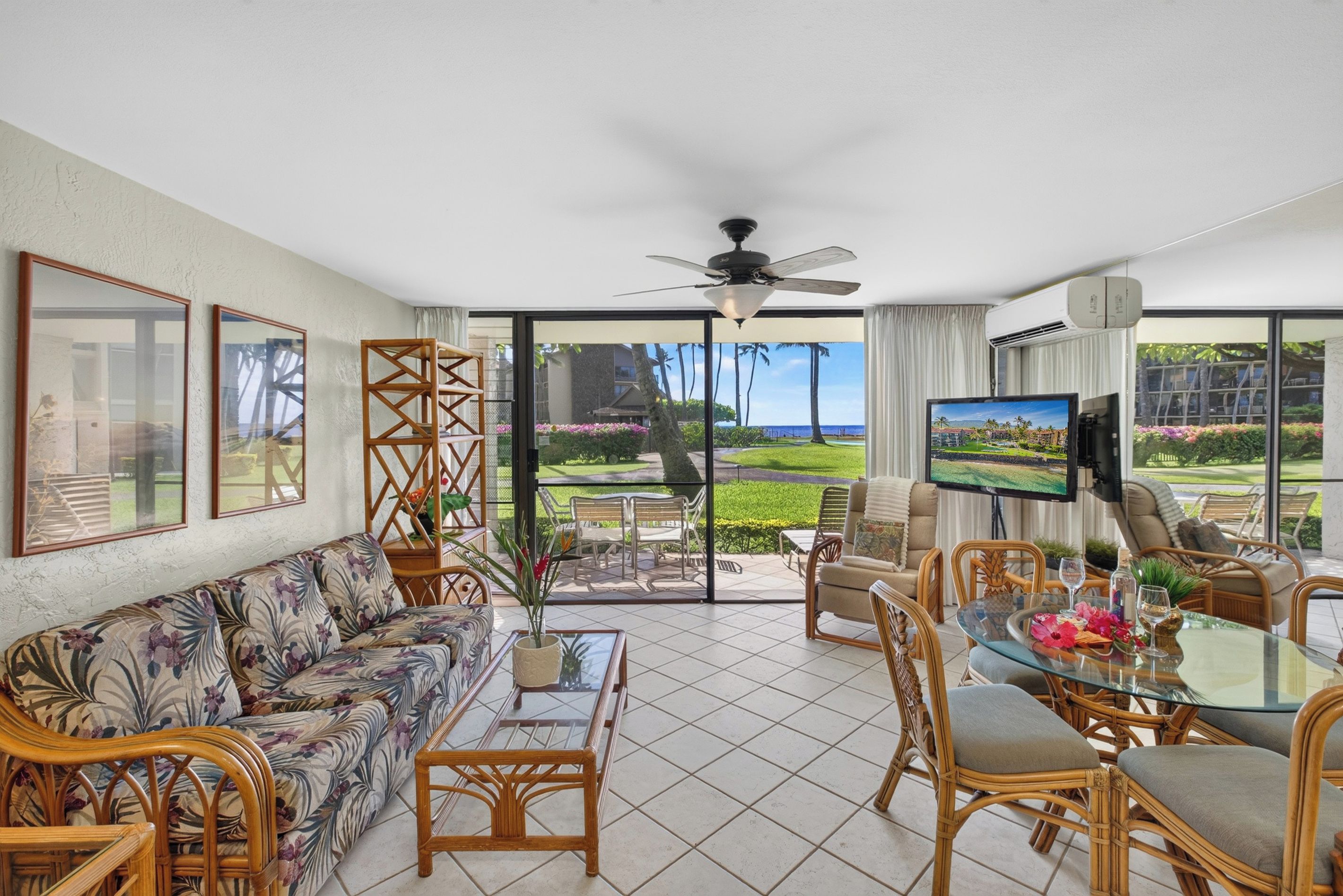 A spacious living room with a large window, a ceiling fan, and a flat-screen TV.