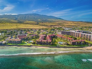 An aerial view of a resort with multiple buildings, a beach, and clear turquoise waters. - Oceanfront Ground-Floor Retreat at Papakea B108 (Lahaina)