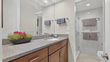 A modern bathroom with a granite countertop, wooden cabinets, a large mirror, and a glass-enclosed shower.
