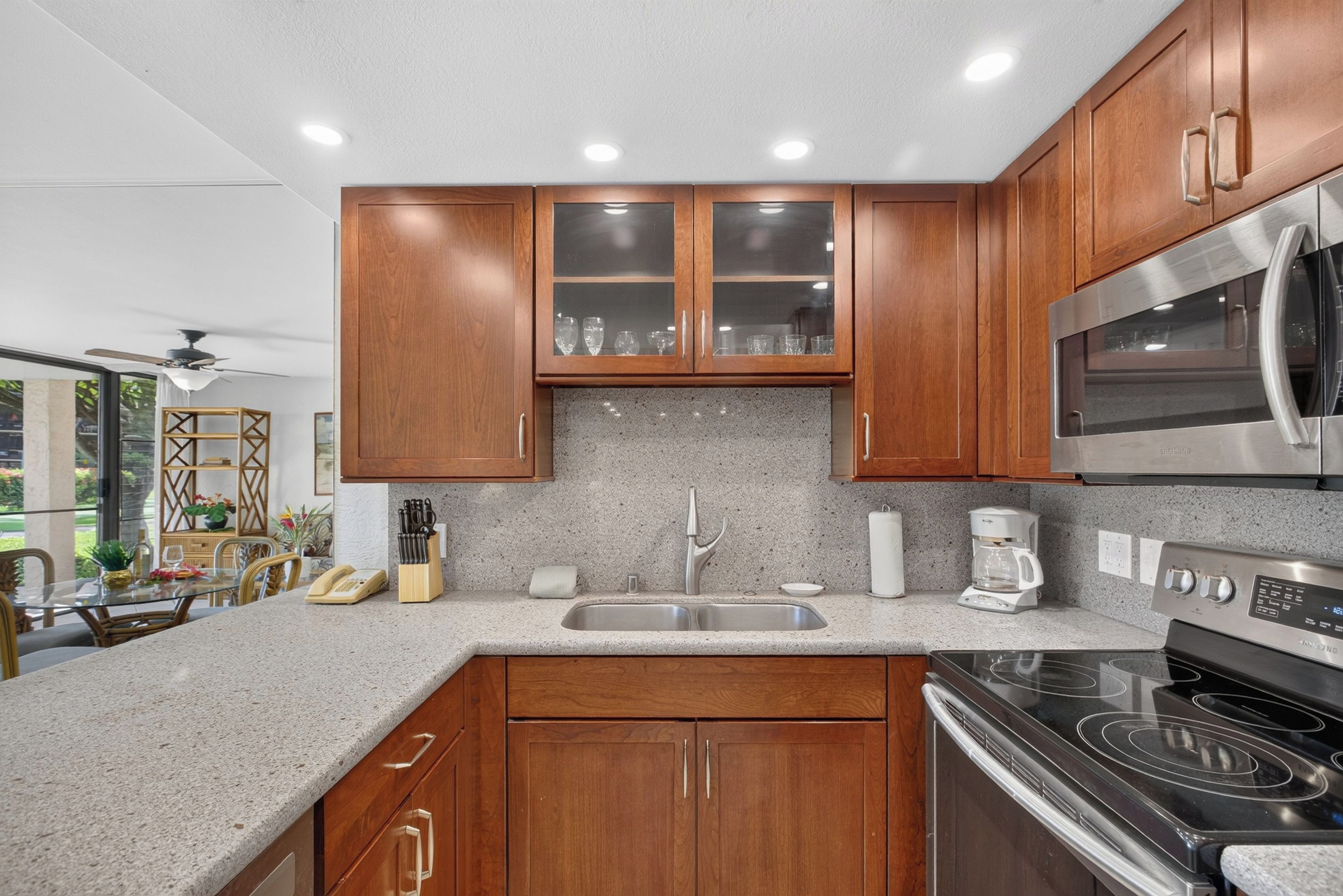 A modern kitchen with wooden cabinets, a stainless steel microwave, a built-in oven, and a granite countertop.