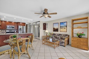 A modern kitchen with stainless steel appliances, a dining area with wicker furniture, and a living room with a sofa and a ceiling fan. - Oceanfront Ground-Floor Retreat at Papakea B108 (Lahaina)