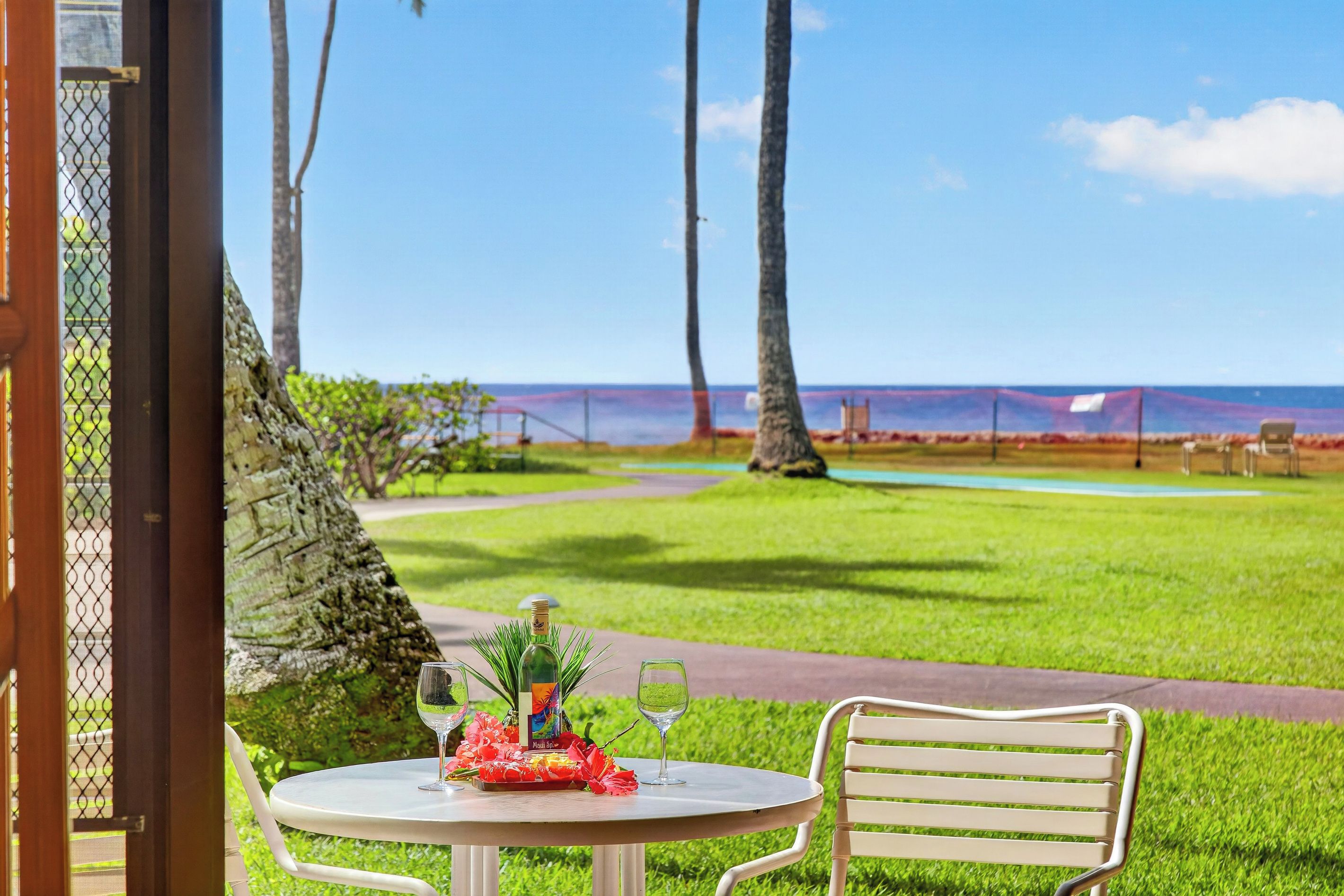 An outdoor seating area with a table set for two, overlooking a grassy landscape and the ocean.