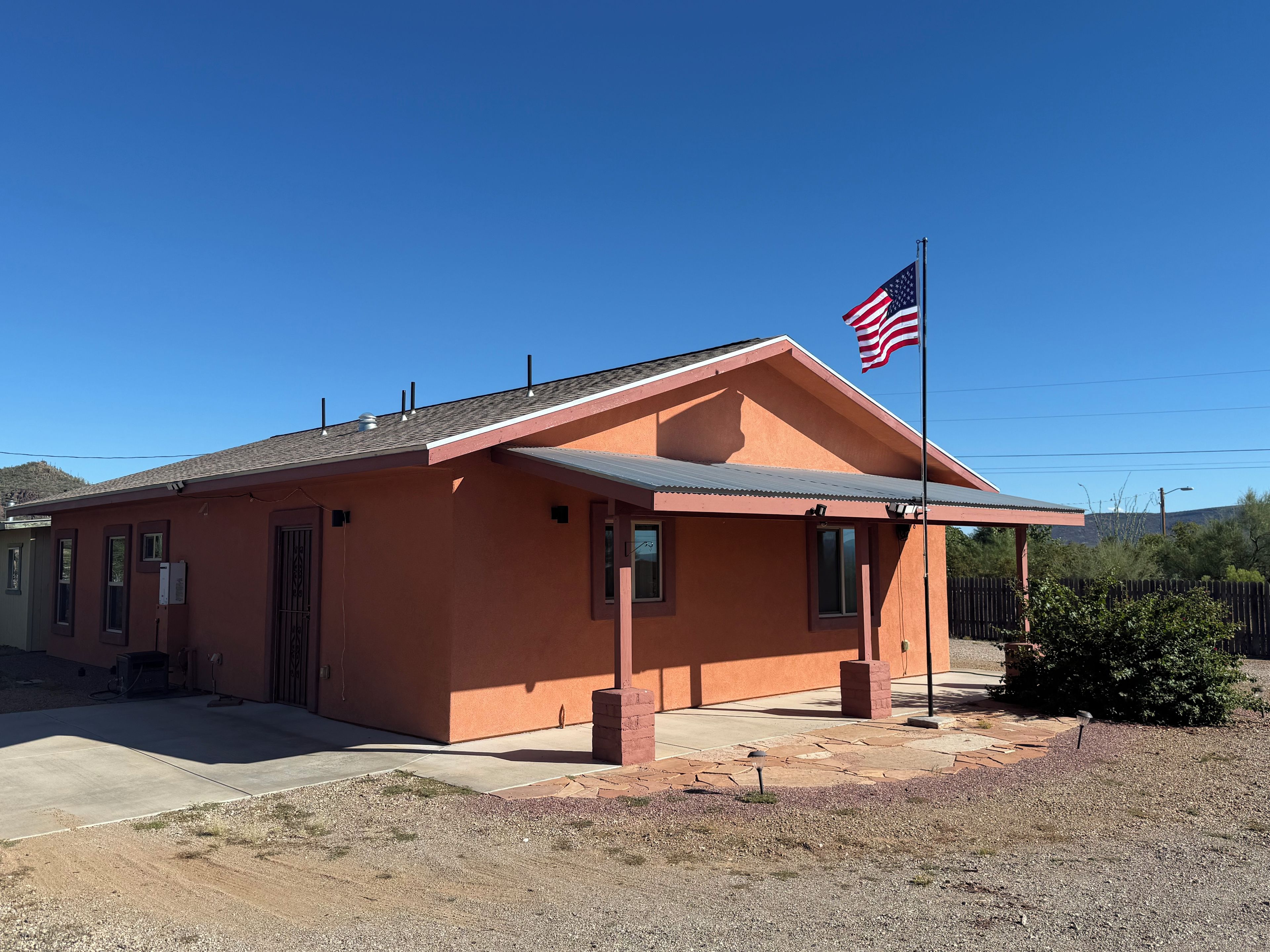 A single-story building with a flat roof, a flagpole with an American flag, and a clear blue sky.