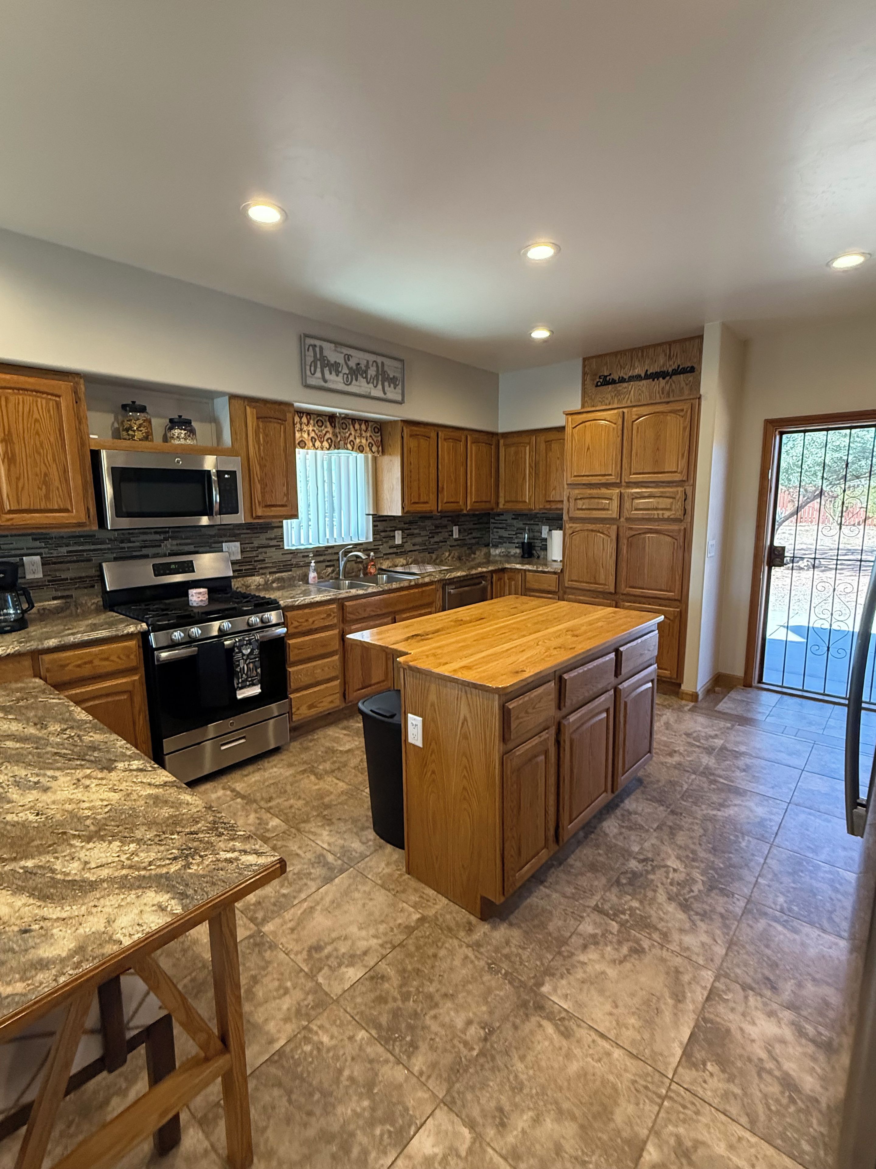 A modern kitchen with wooden cabinets, a central island, stainless steel appliances, and a view to the outside.
