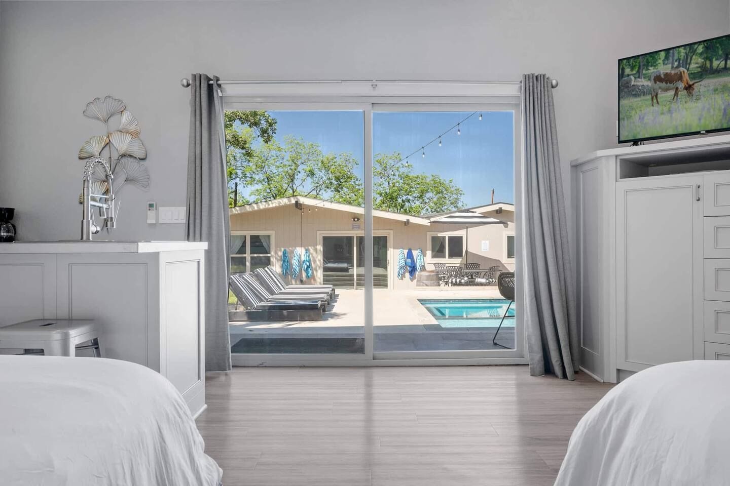 A hotel room with a sliding glass door leading to a pool area, a television on the right, and a bed on the left.