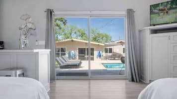 A hotel room with a sliding glass door leading to a pool area, a television on the right, and a bed on the left.