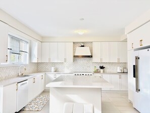Une cuisine moderne avec des meubles blancs, un îlot central, un four encastré et un réfrigérateur en acier inoxydable.