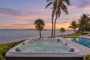 A hot tub with a city skyline and palm trees in the background. - Bayfront 6BR Compound | Pool, Hot Tub & Views (Miami)
