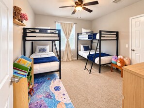 A bedroom with bunk beds, a ceiling fan, a window with curtains, and a bookshelf with books and stuffed animals. - Cedar Park Oasis - Pool, Movie & Game Room, BBQ, Sleeps 18 (Cedar Park)
