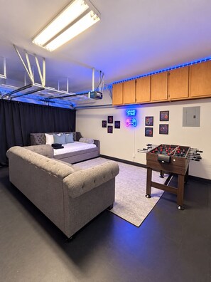 A room with a sofa, a bed, a foosball table, and a neon sign. - Cedar Park Oasis - Pool, Movie & Game Room, BBQ, Sleeps 18 (Cedar Park)