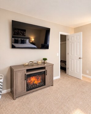 A room with a fireplace, a bed with a headboard, a mirror, and a door leading to another room. - Cedar Park Oasis - Pool, Movie & Game Room, BBQ, Sleeps 18 (Cedar Park)
