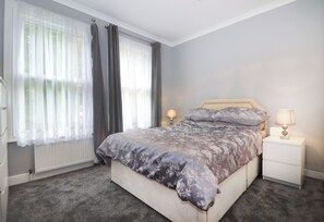 Ein Schlafzimmer mit einem Bett, zwei Nachttischen, einem Fenster mit Vorhängen und einer Heizung.