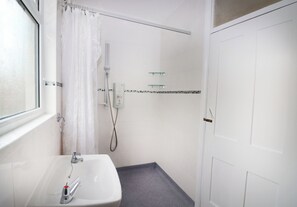 Ein Badezimmer mit einem weißen Waschbecken, einer Dusche mit Ablagefläche aus Glas und einer weißen Tür.