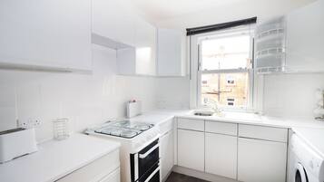 Eine moderne Küche mit weißen Schränken, einem eingebauten Ofen, einem Gasherd und einem Fenster mit Blick auf ein Ziegelgebäude.