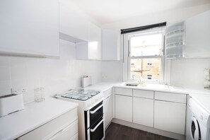 A modern kitchen with white cabinetry, a built-in oven, a gas stove, and a window with a view of a brick building.