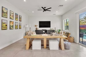 A dining area with a wooden table, white cushioned benches, a black ceiling fan, and a large flat-screen TV mounted on the wall. - Heated Pool & Spa, Golf Simulator, Billiards - Walking Distance to Old Town (Scottsdale)