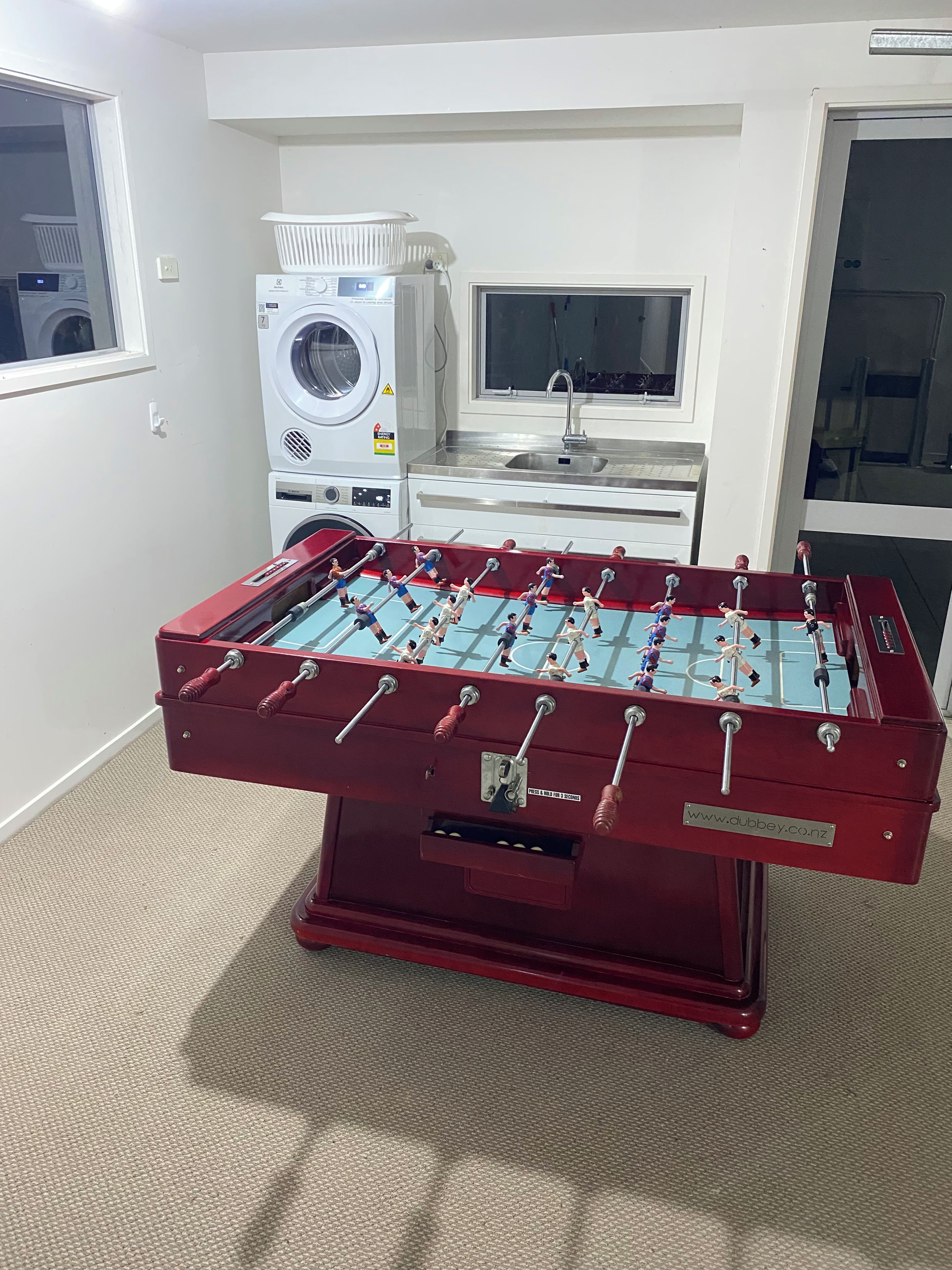 Ein Zimmer mit Tischfußball, einer Waschmaschine und einem Waschbecken.