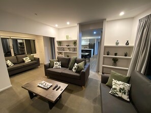 A modern living room with a sofa, a coffee table, and a dining area in the background.