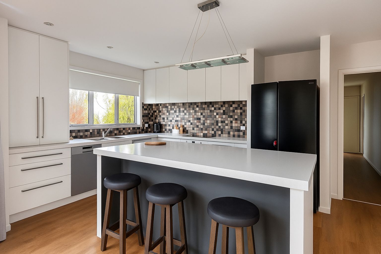 Eine moderne Küche mit weißen Schränken, einer großen Kochinsel mit Sitzgelegenheiten, einem schwarzen Kühlschrank und einer gemusterten Spritzschutzwand.