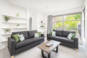 A modern living room with two grey sofas, a wooden coffee table, and white shelving units.