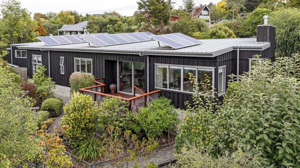 Une maison moderne dotée de panneaux solaires, de grandes fenêtres et d’une terrasse en bois.