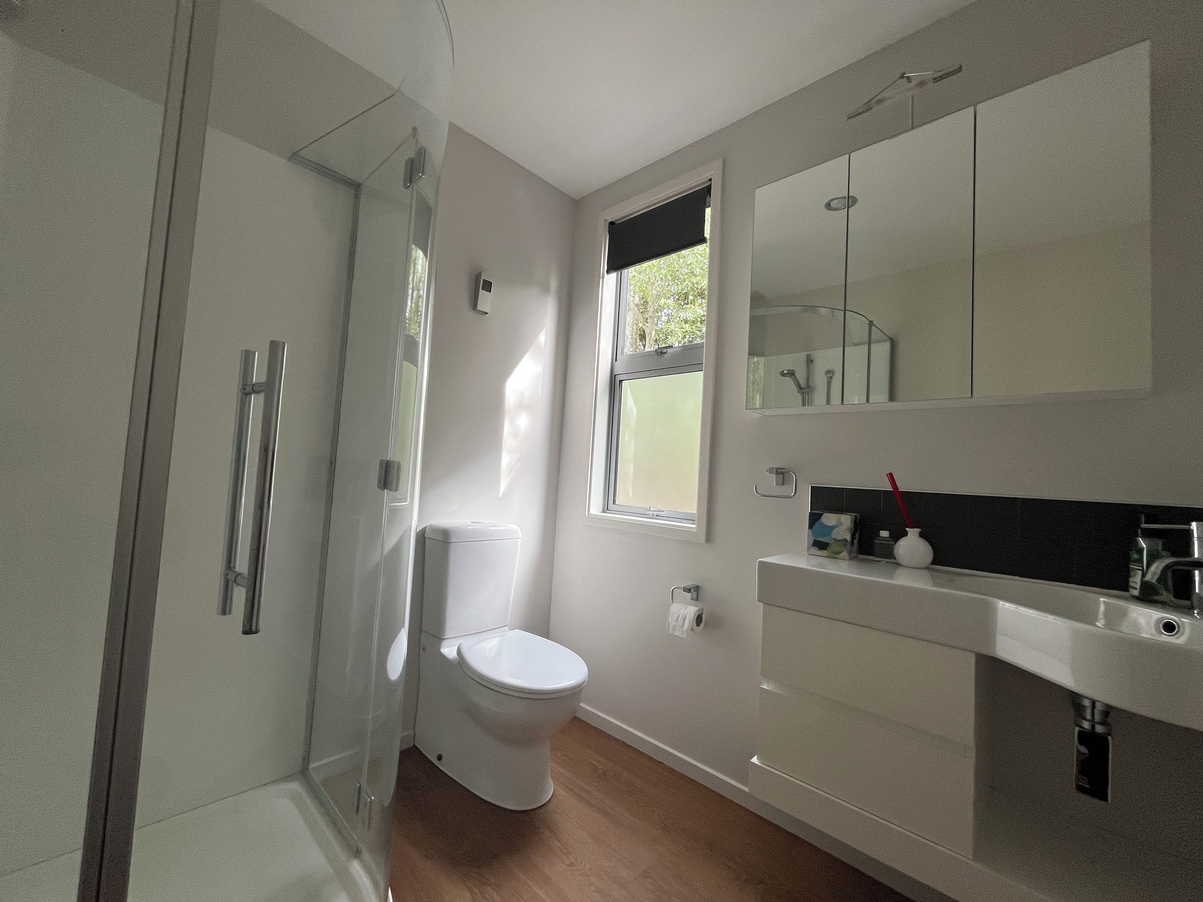 Un baño moderno con cabina de ducha de vidrio, inodoro, lavamanos con espejo y ventana.