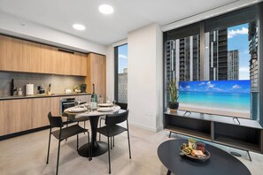 Eine moderne Küche mit Holzschränken, ein Essbereich mit rundem Tisch und Stühlen sowie ein großes Fenster mit Blick auf die Stadt.