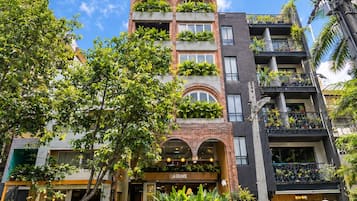 Un edificio de varios pisos con balcones, acceso al nivel de la calle y un restaurante visible con mesas al aire libre.