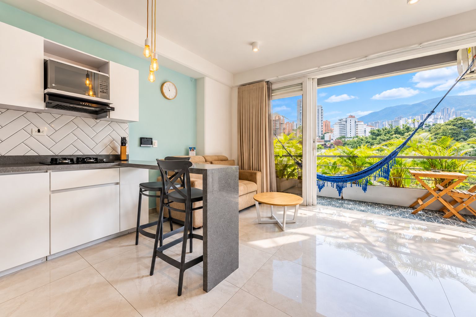 A modern kitchen with a dining area, a living space with a view, and a balcony with a hammock.