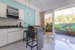 Una cocina moderna con salpicadero de azulejos tipo espiga, microondas integrado y cocina a gas. Hay una zona de estar con sofá y una mesa redonda pequeña, y un balcón con una hamaca.